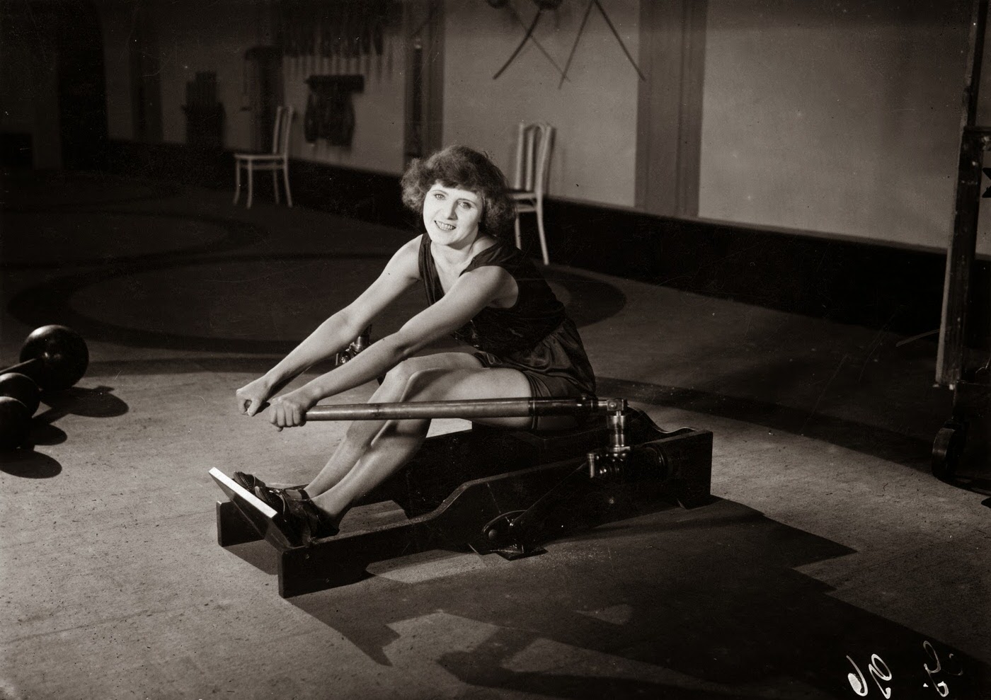 A woman exercising on a rowing machine in impractical shoes, circa 1920.