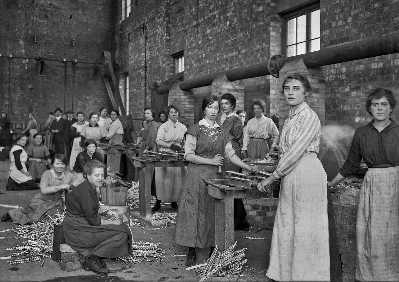 A group of manual workers, mostly women, inside a factory, WW1 era.