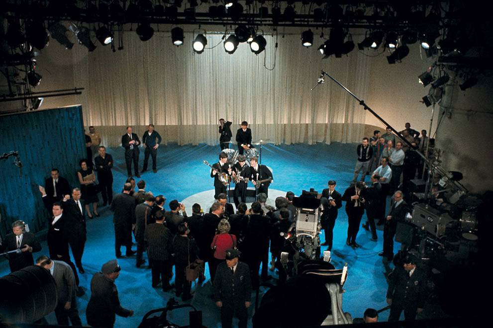 The Beatles surrounded by photographers on stage at CBS' Studio 50 before their live television appearance on The Ed Sullivan Show in New York City, 1964.