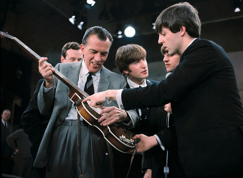 Paul McCartney shows his guitar to Ed Sullivan before the Beatles' live television appearance in New York; Beatles manager Brian Epstein, John Lennon, and Ringo Starr are behind Sullivan, 1964.