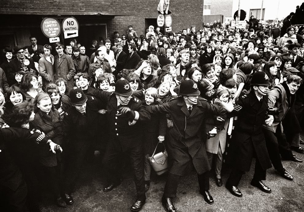 Policemen good-humoredly control screaming Beatles fans as the Liverpool pop group were welcomed by a group of more than 5,000 on their arrival at London Airport on their return from America, 1964.
