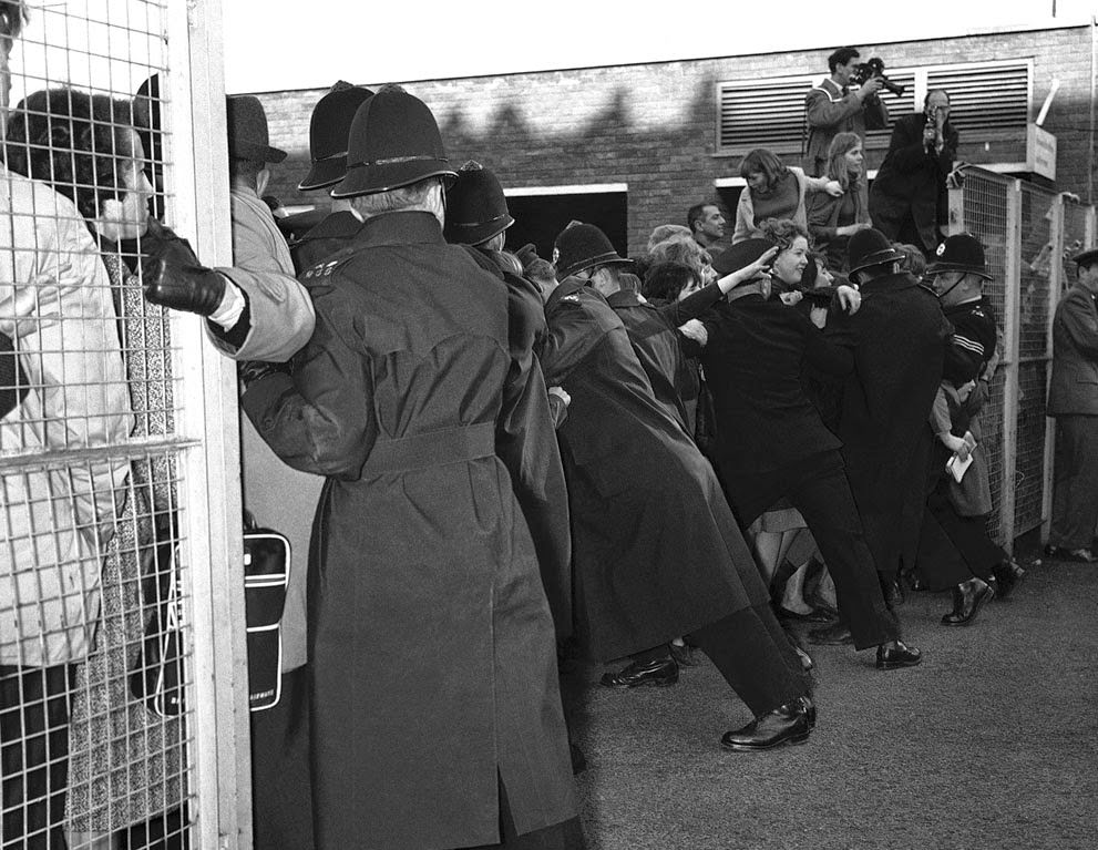 Police hold back screaming fans fighting to get near the Beatles, when the Liverpool pop group returned to London Airport from Paris, 1964.