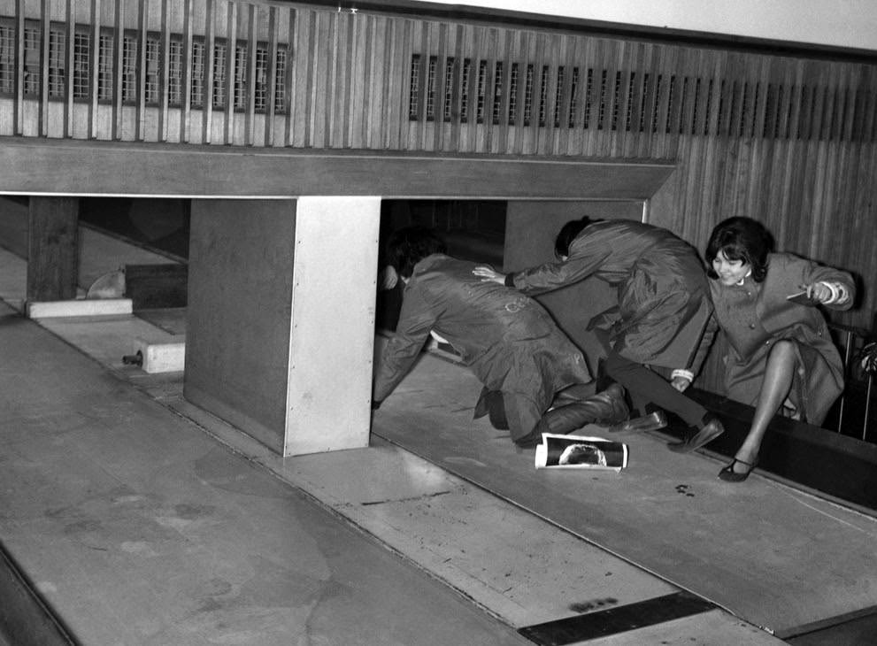 Three Beatles fans attempt to enter the Customs Hall at London Airport by crawling into the baggage conveyor belt, 1964.