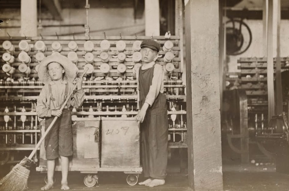 Ronald Webb, twelve year old doffer boy and Frank Robinson, seven year old who helps sweep and doff. Father is cardroom boss, Roanoke (Va.) Cotton Mills. Roanoke, Virginia, USA, May 1911.