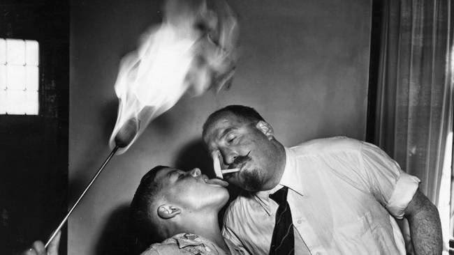 A young fire-eater gives his father a light from his tongue.