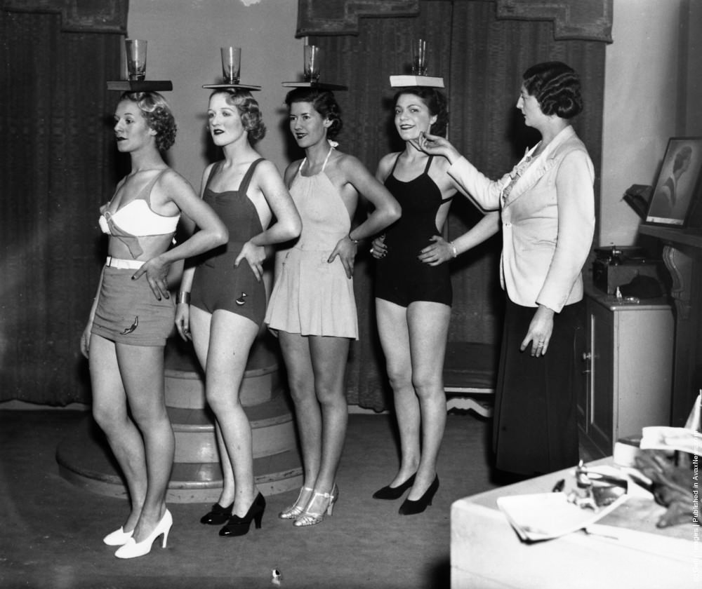 Lucie Clayton instructs pupils in the art of correct posture by balancing a glass and book on their heads at her finishing school in Old Cavendish Street, London, 1936.