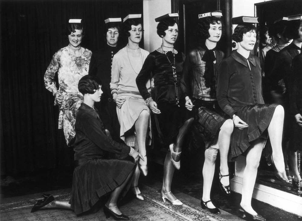 Trainee fashion models learn how to carry themselves gracefully by balancing books on their heads at a school of modelling and deportment in the West End of London, 1925.