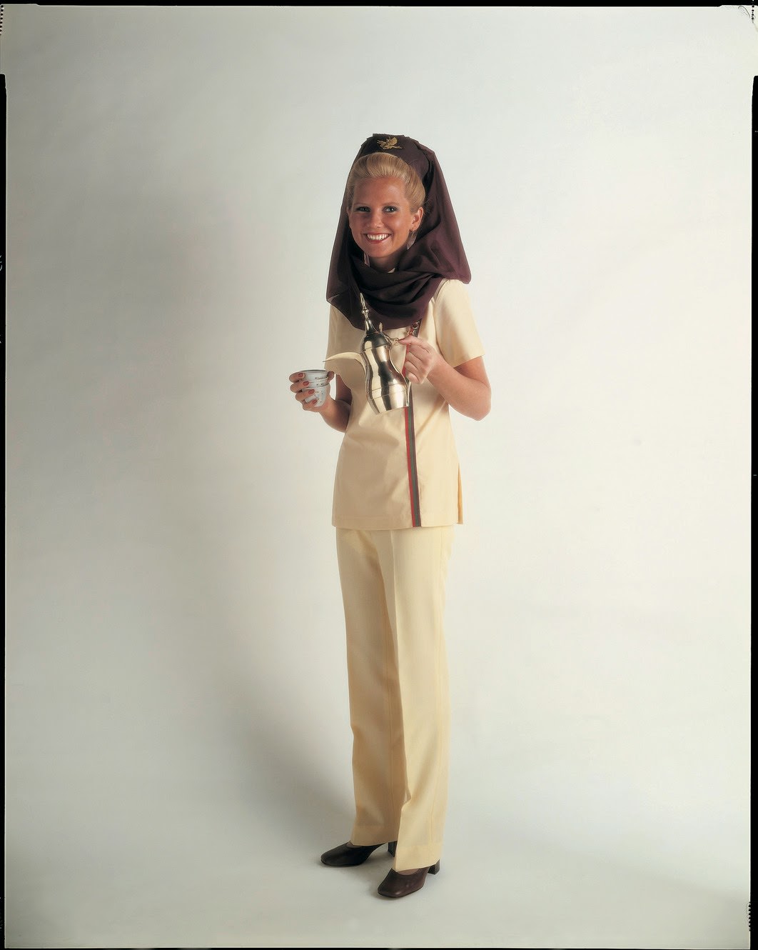 Middle East meets West in the 1970s with Gulf Air's adaptation of the Muslim headdress; legs are covered by smart trousers. The uniform was originally designed by Joy Stokes.