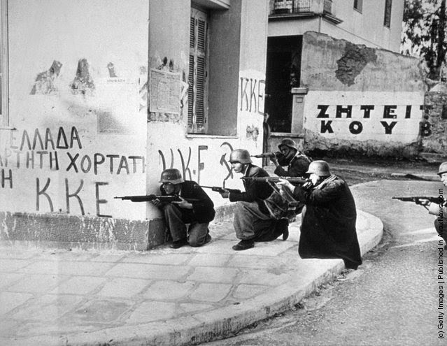Steel-helmeted Elas troops use a corner building as a shelter as they fire at police headquarters during a civil uprising in Athens, 1944.