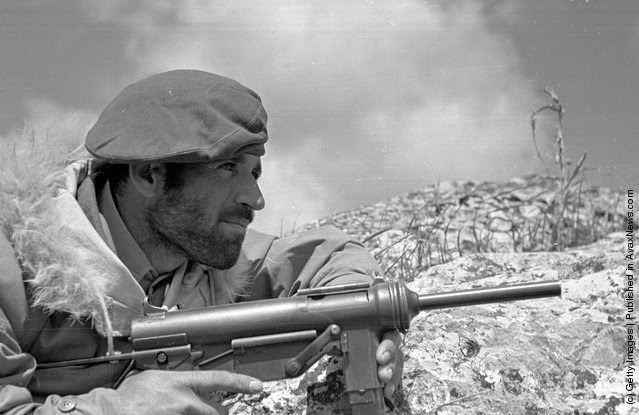 A Greek commando soldier, wearing a fur-collared jacket supplied by the Americans, waits for a guerrilla target to emerge during the Greek Civil War, 1948.