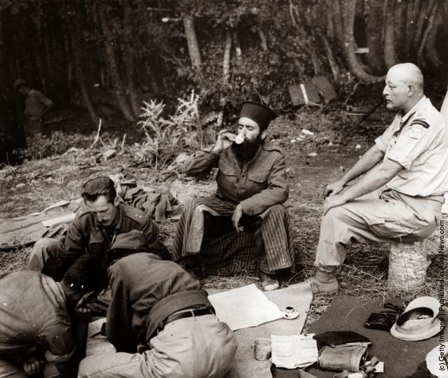 Officers plan the assault on Mount Kiapha at Mount Lyoku during the Greek Civil War, while a Greek Orthodox priest drinks coffee; each brigade has a chaplain who travels with them, 1947.