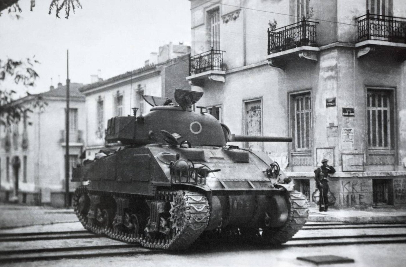 Soldiers of the 23rd Armoured Brigade in Petmeza Street, Athens, during the Dekemvriana; the Sherman tank is from C Squadron, 46th Royal Tank Regiment and the soldier stands besides graffiti from the KKE, 1944.
