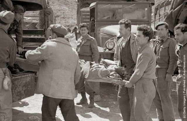 A group of soldiers loading a wounded man on a stretcher into a van during the Greek Civil War, 1948.