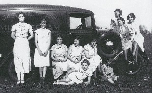 Catherine Emery, mother of nine daughters, seated with chin in hand, assisted with morning milk deliveries for Chesterfield Dairy with her daughters before they headed off to school, 1930s.