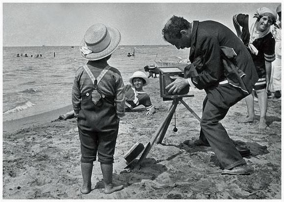 French photographer on a beach with a very interested lad who one day might take on the role of a fashion photographer.