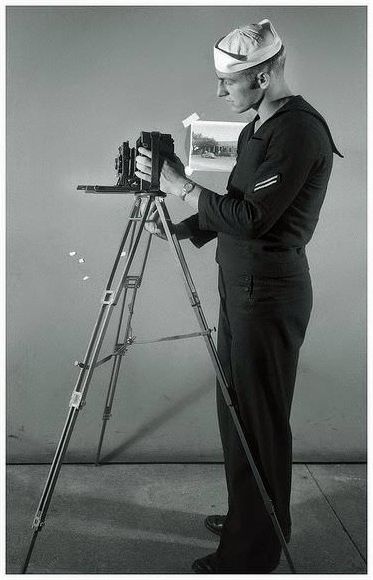A United States Navy photographer undergoes training with a large format press camera during World War II.