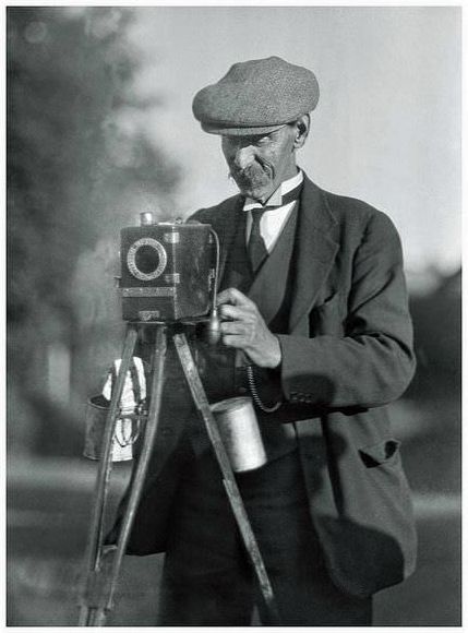 A street photographer, somewhere in England, with his Moore & Co Aptus Ferrotype camera. The processing solutions hang from the struts of his wooden tripod.