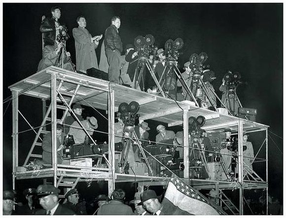 Press and Television corps at MacArthur Day commemorations in Chicago during the late 1940's. A battery of different cameras, including Arriflex and Mitchell movie cameras, and Graflex 'Big Bertha' cameras, are being operated by photographers and cameramen from NBC, and Chicago's WGN-TV, as well as the Chicago Sun Times.