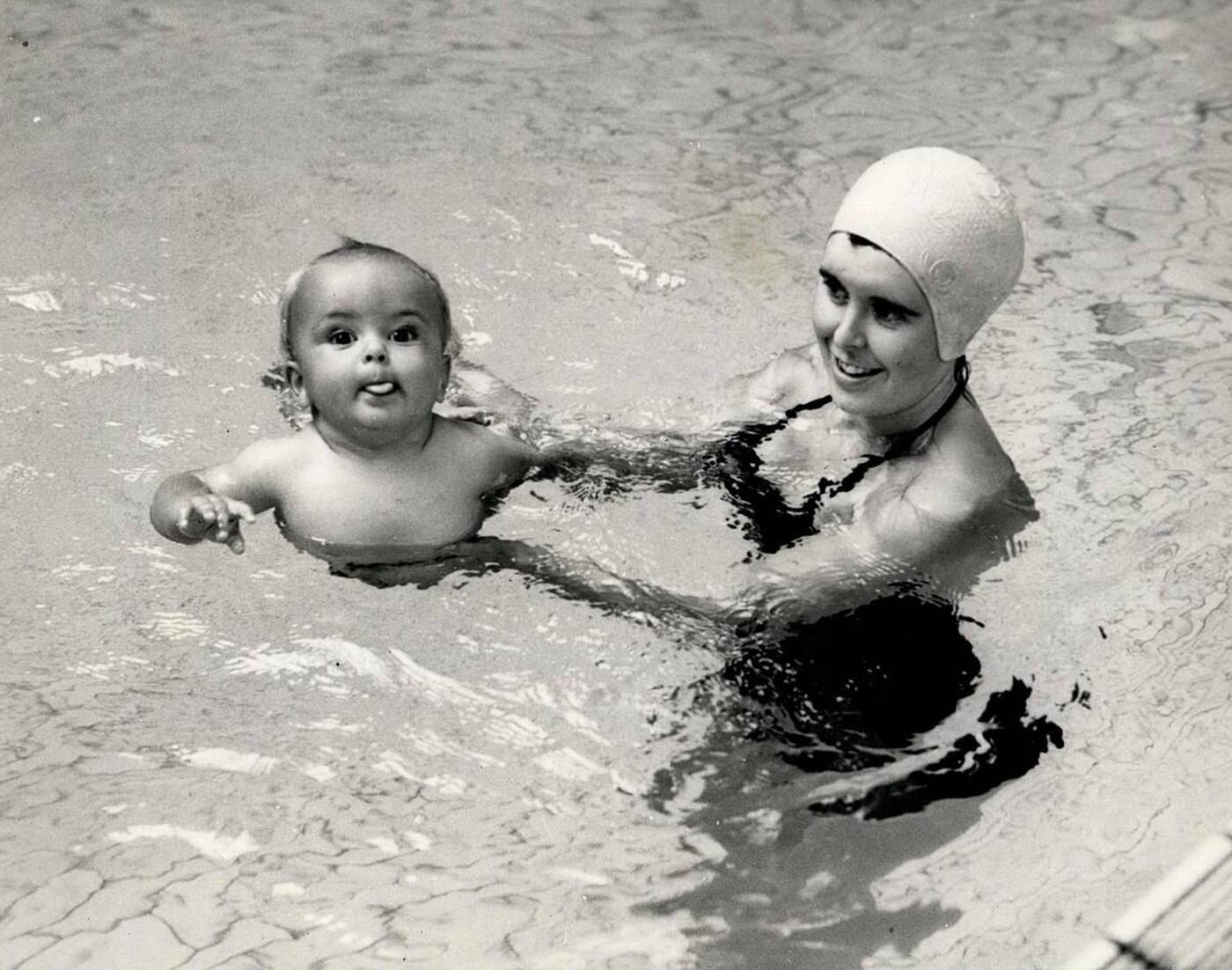 Bobbie, a nine-month-old son of a P.T. instructor, is supported by his mother as he tries a few strokes in the Royal Marine Swimming Bath at Deal, Kent, 1960.