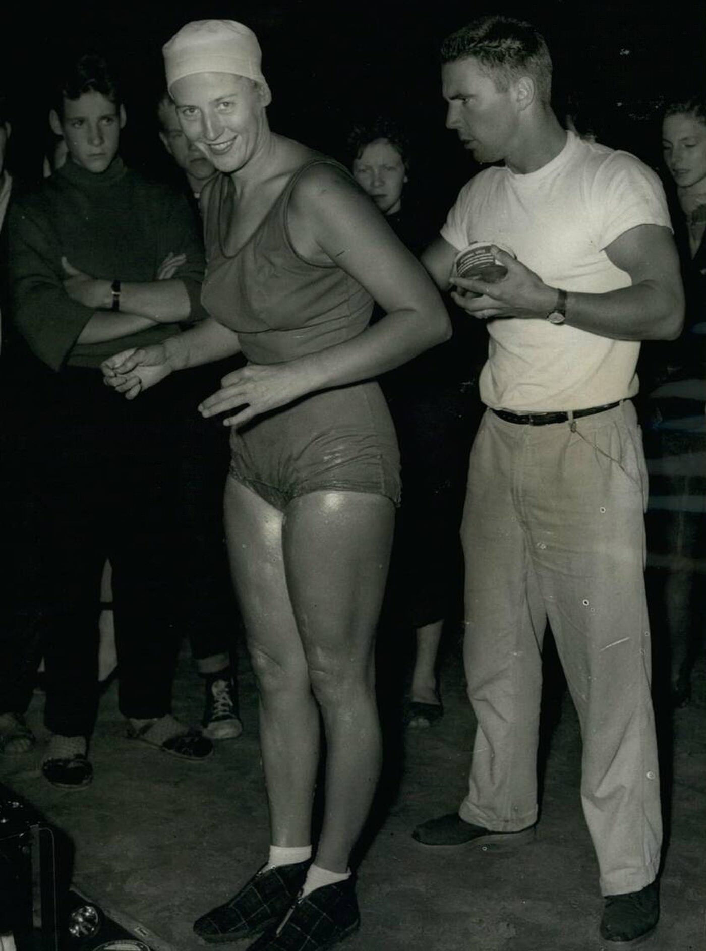 Greta Anderson is greased by her husband P.T. Instructor John Sonnichsen before she entered the water to win the International Cross Channel Swimming race, 1958.