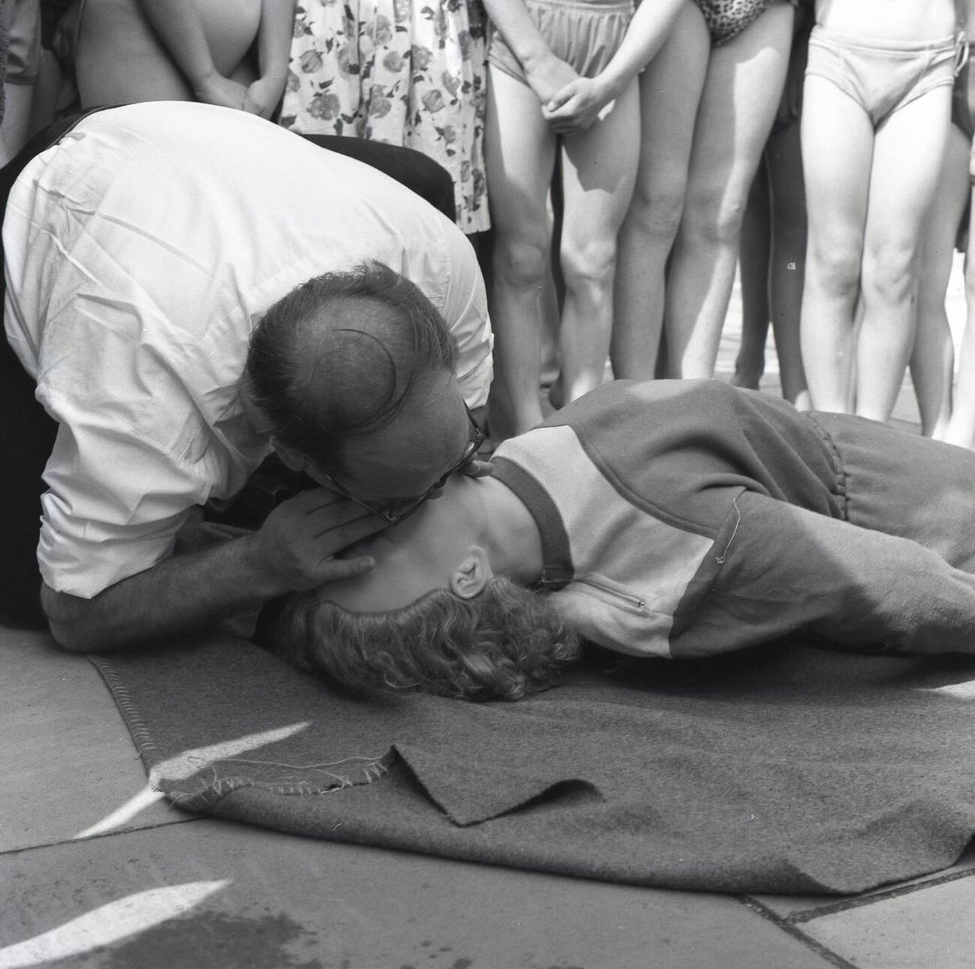 An instructor demonstrates the 'kiss of life' to a training dummy as part of a life-saving demonstration for junior swimmers at Vale Pool, an open-air swimming pool in Aylesbury, Bucks, England, 1964.