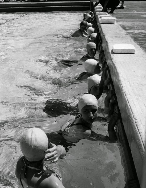 These schoolgirls are clinging to the pool wall, kicking furiously, during a swimming lesson on June 19, 1962.