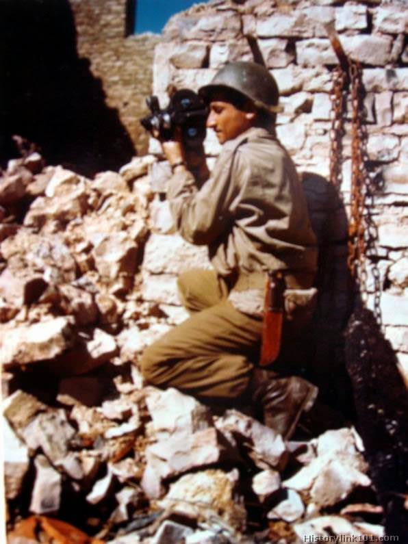 An Army Signal Corps photographer perches atop a pile of rubble to film the battle for Normandy, 1944.