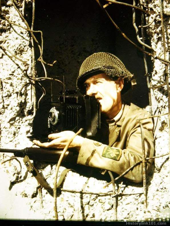 A combat cameraman uses an old shattered German pillbox for protection while photographing the war action, after being in the ETO for 27 months.