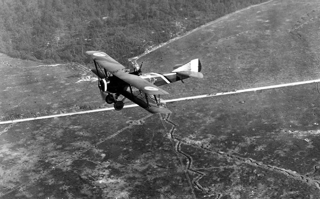 A French SPAD S.XVI two-seat biplane reconnaissance aircraft flying over Compeign Sector, France, with zig-zag patterns of defensive trenches in the fields below, 1918.