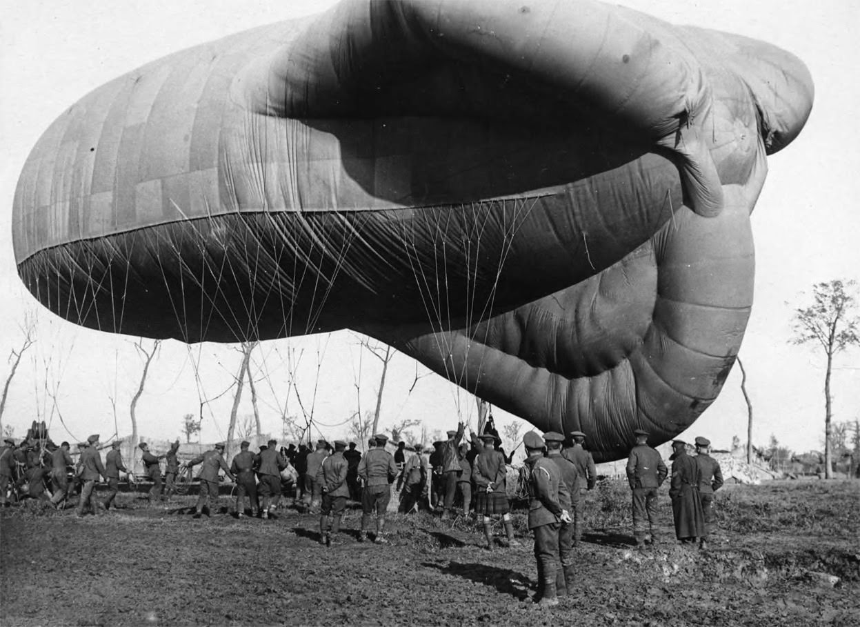 A returning observation balloon being controlled by soldiers with ropes; the basket attached to the balloon can be seen on the ground.