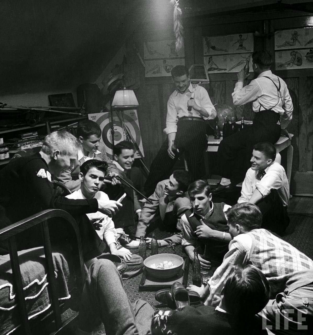 Teenage boys hang out in friend's bedroom, drinking Cokes, eating potato chips with assorted paraphernalia - gun, bow and arrows, pinups - visible around the room, Des Moines, Iowa.
