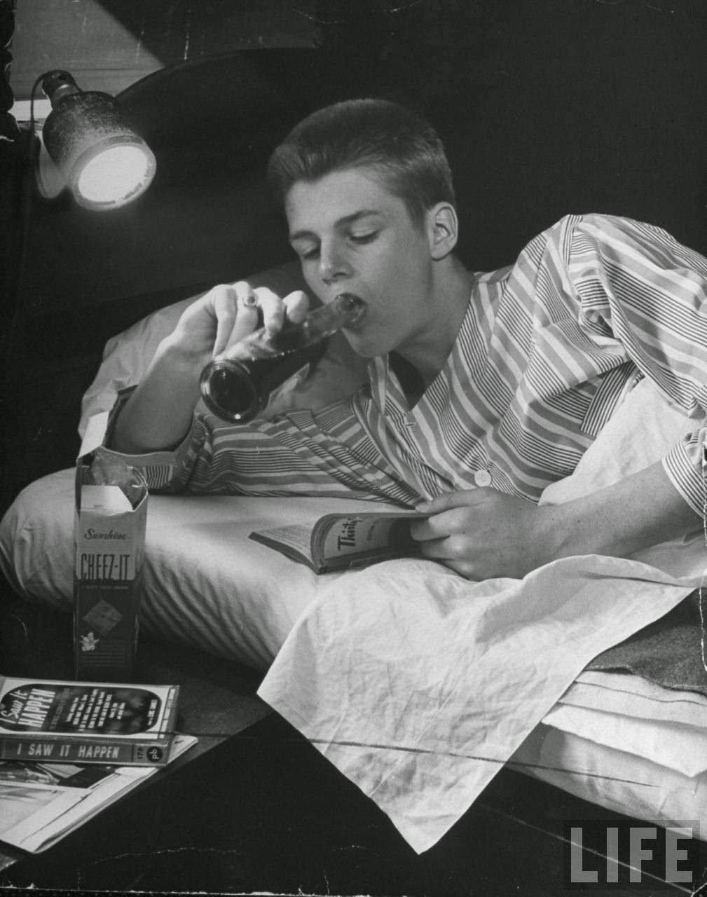 Teen-age boy drinking coke and eating crackers in bed.