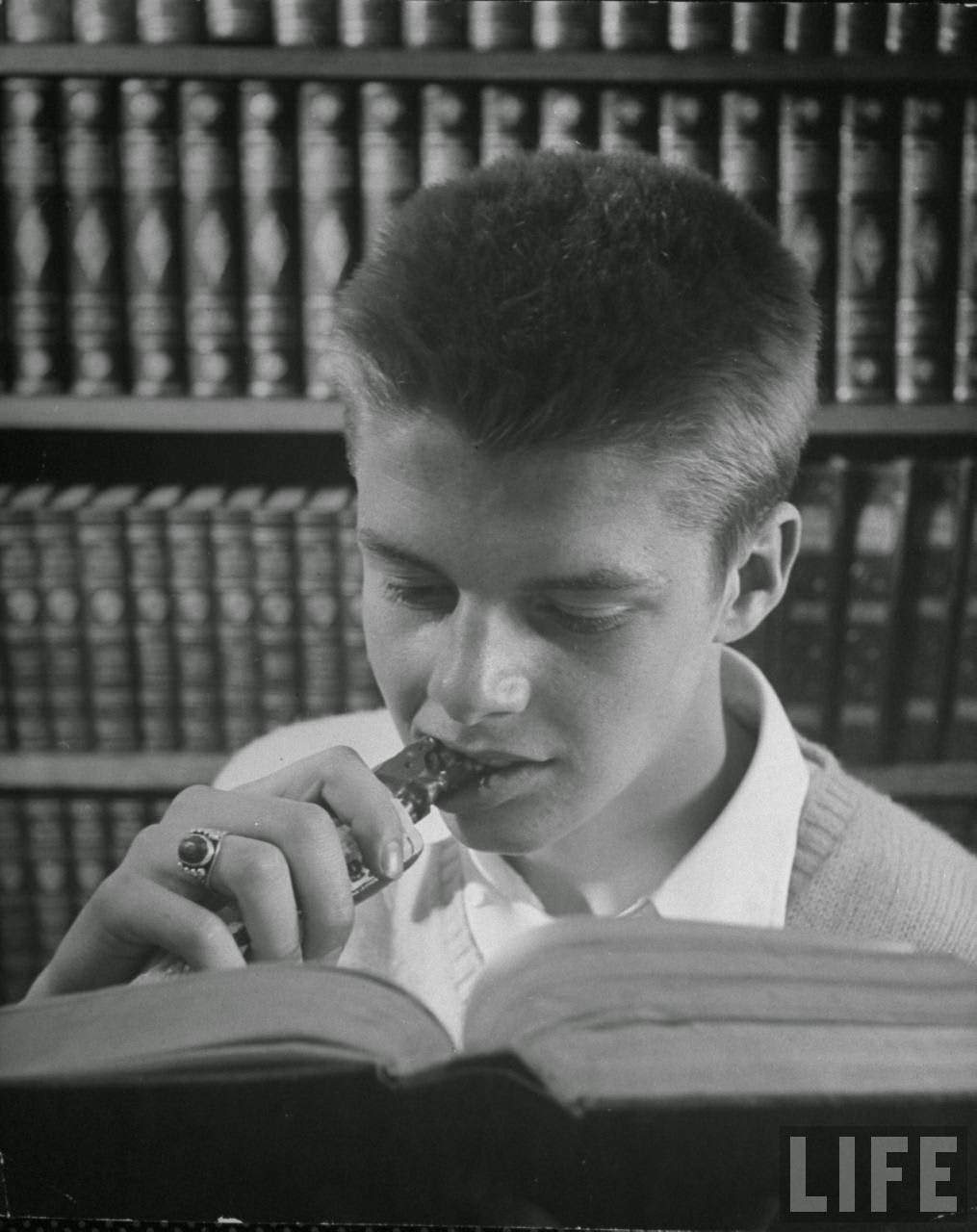 Boy eating candy bar in school and getting away with it is quite a trick, usually done under cover of school book.