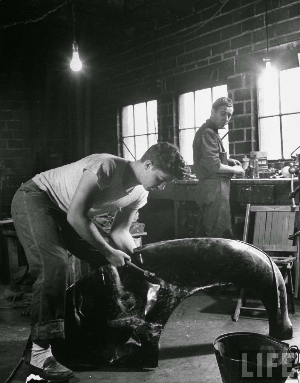 Teen-age boy in garage with father fixing a smashed fender.