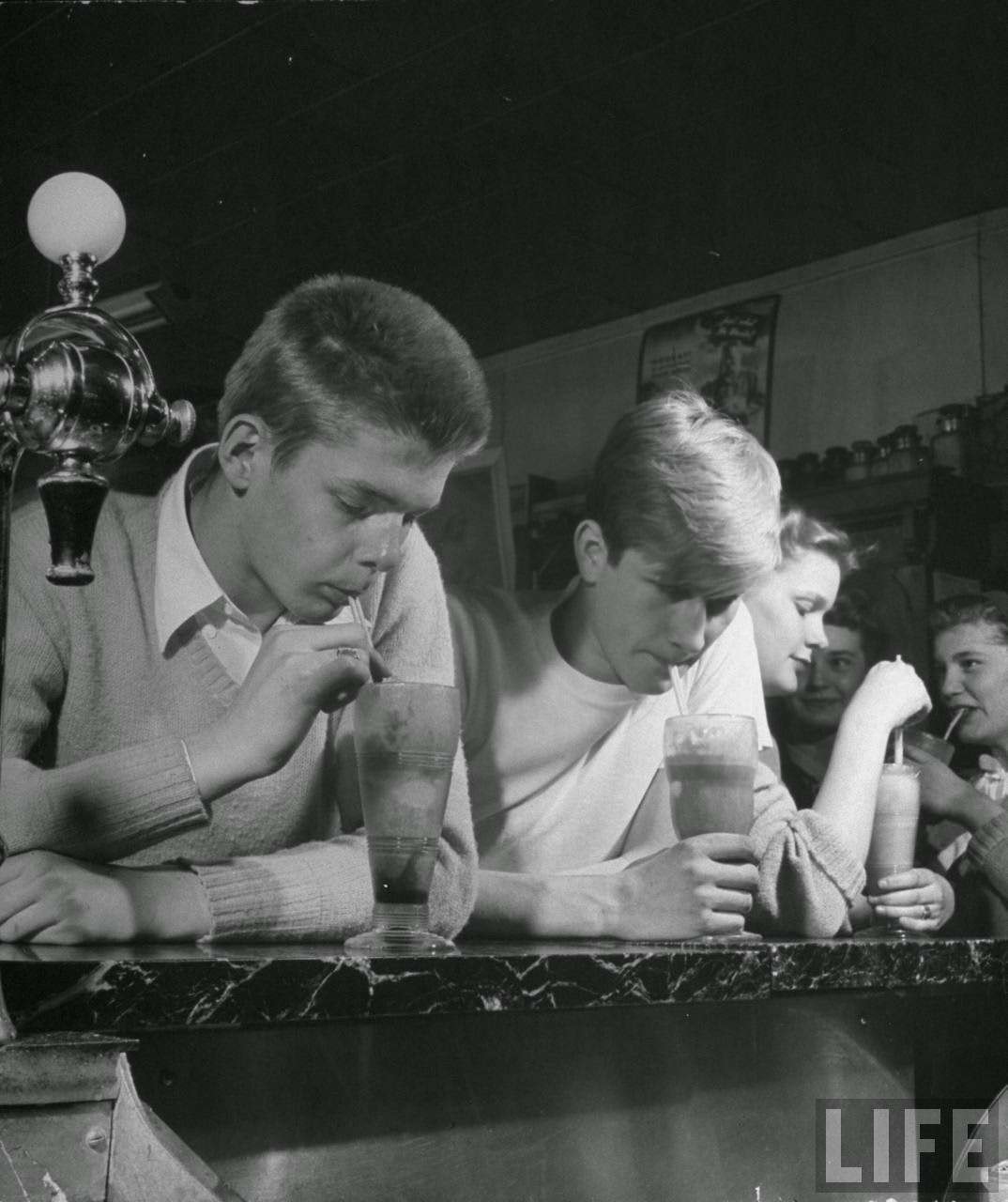Teen-age boys and girls drinking milkshakes in drug store.