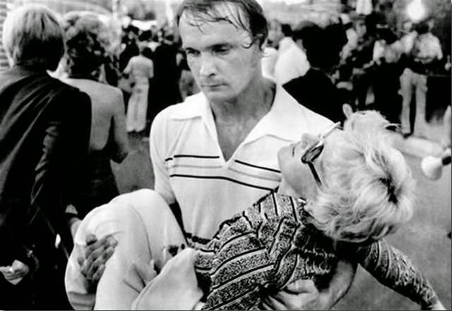 An exhausted volunteer carries a victim of the heat and confusion to a first aid station inside the gates of Graceland Mansion in Memphis, where thousands gathered for a chance to view Elvis Presley's body.