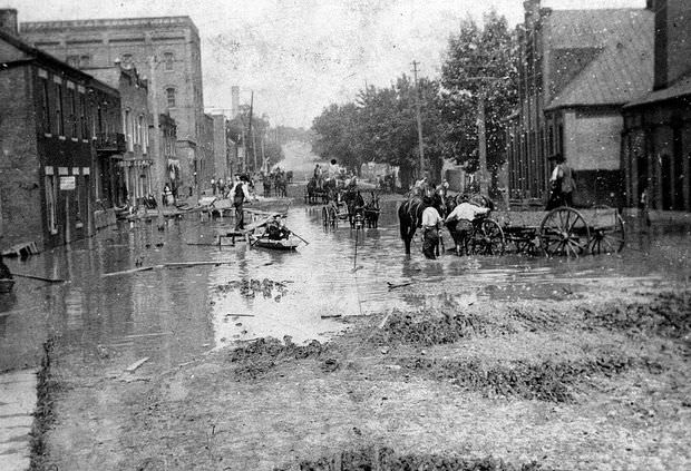 Men in boats or horse-drawn wagons navigate a flooded area of Jefferson City, Missouri, 1903
