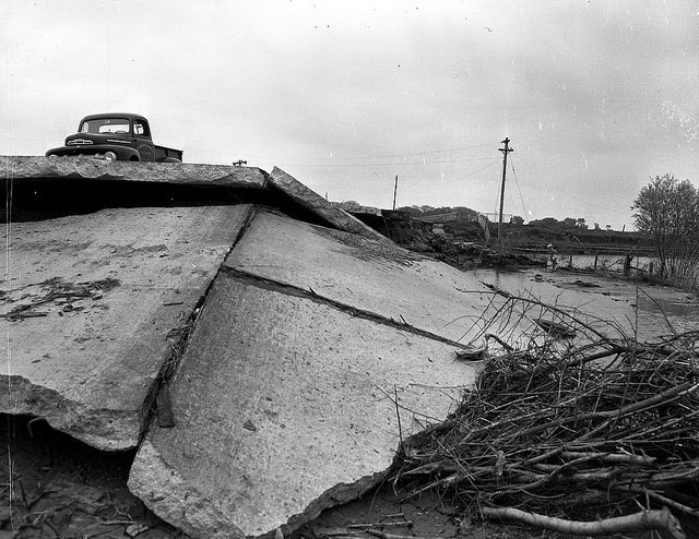 Truck parked atop road concrete warped and damaged by flood waters, 1952