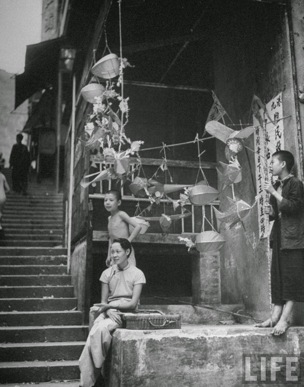 Woman and children selling lanterns and kites in a market on Queen's Road.