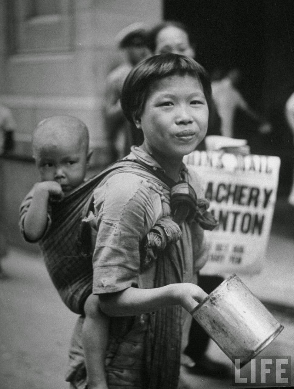 Young girl carrying her baby brother on her back and begging for money.