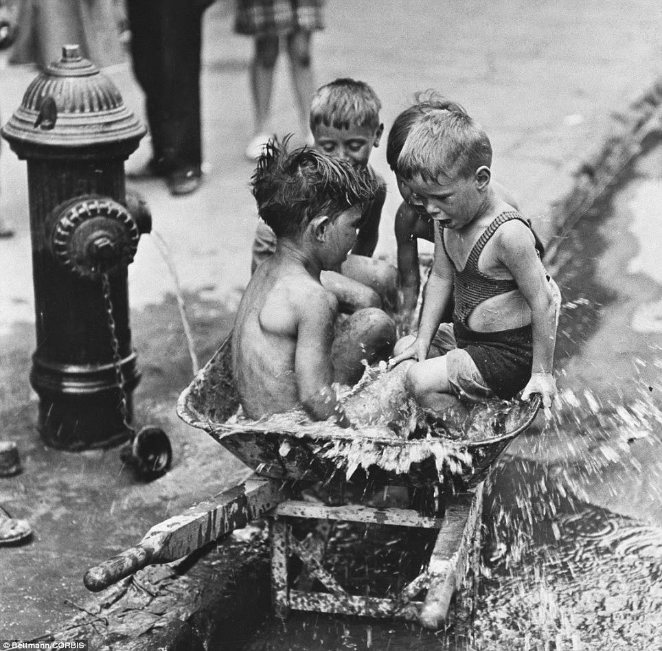 Seated in a WPA wheelbarrow beside a gushing fire hydrant on the Lower East Side, four boys cool off in 95degree heat during 1939