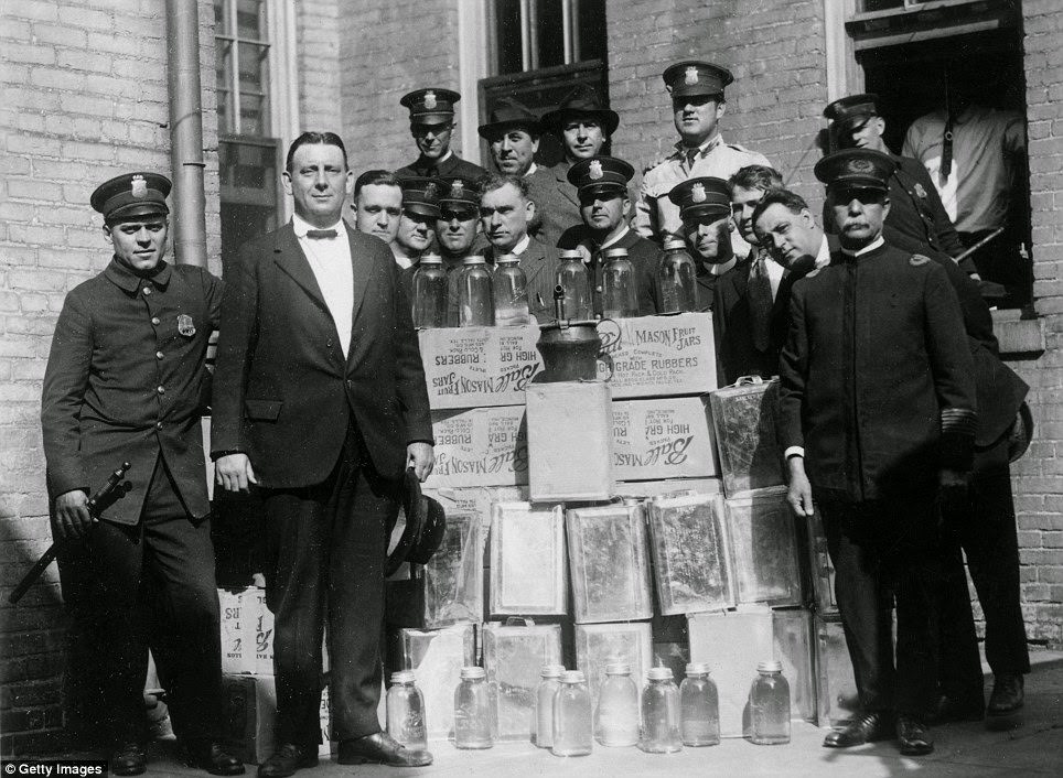 Police pose with cases of illegal alcohol and distilling equipment seized during a raid
