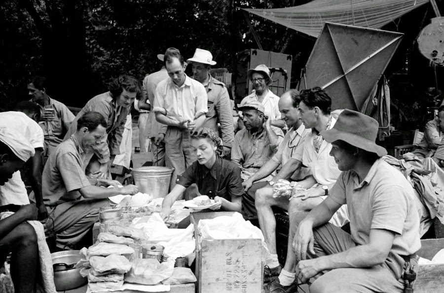Lauren Bacall makes sandwiches while surrounded by her husband and the crew during a lunch break on location for The African Queen.