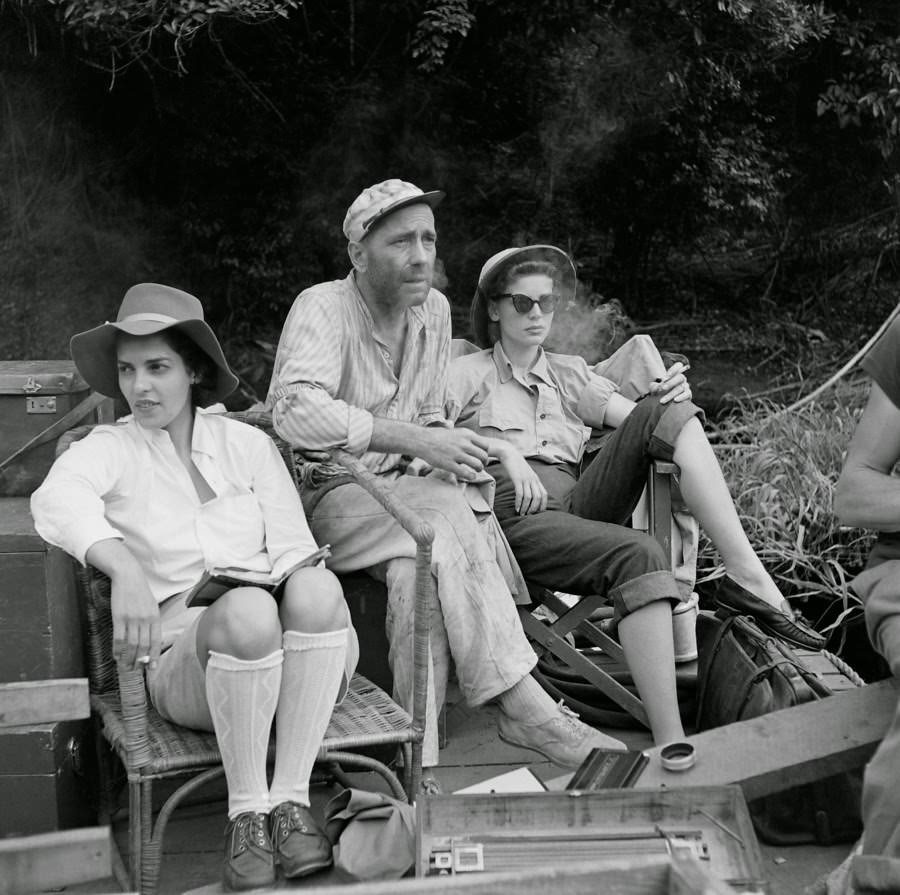 Humphrey Bogart’s wife Lauren Bacall kept him company during production; here, the couple enjoys a smoke with an unidentified woman, 1951.