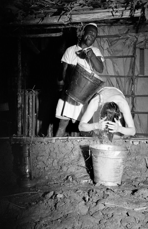 Katharine Hepburn gives her hair its nightly wash on the set of The African Queen, with the help of Sonduco, a production employee.
