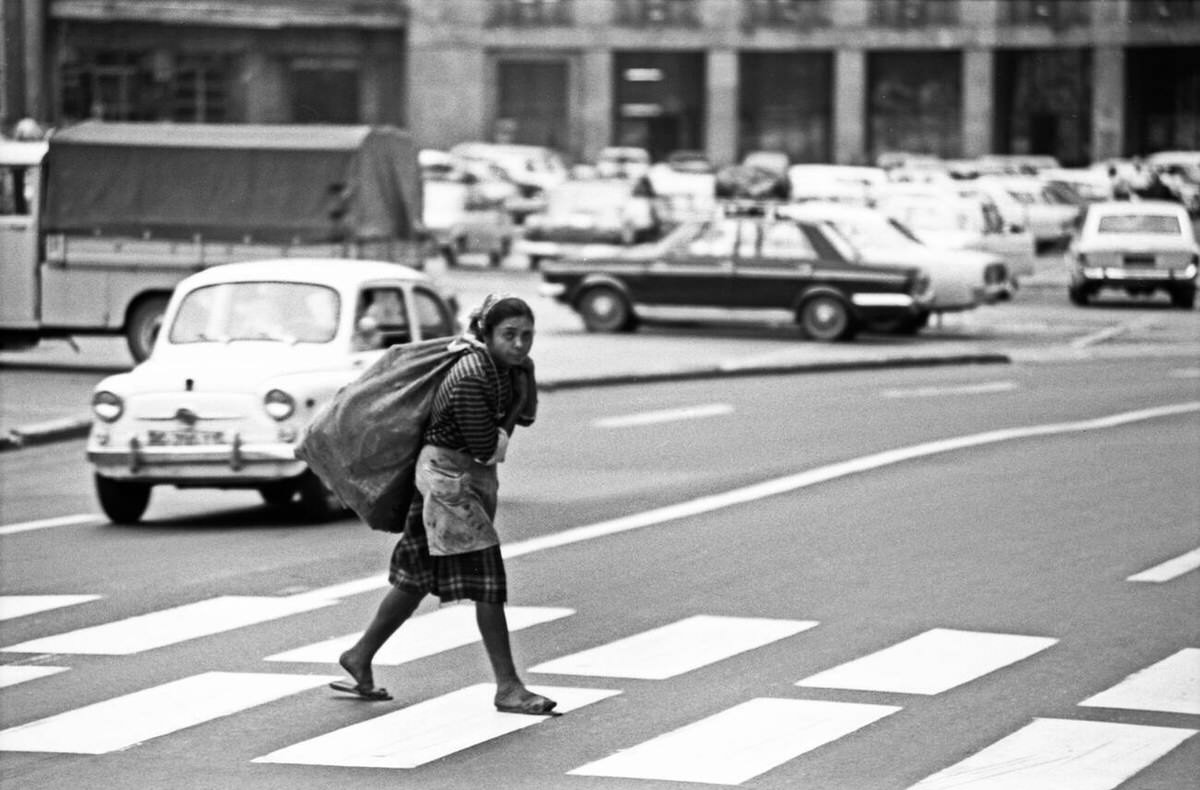 A woman with a bag on her shoulder crosses the street, Belgrade, Yugoslavia, July 1971.