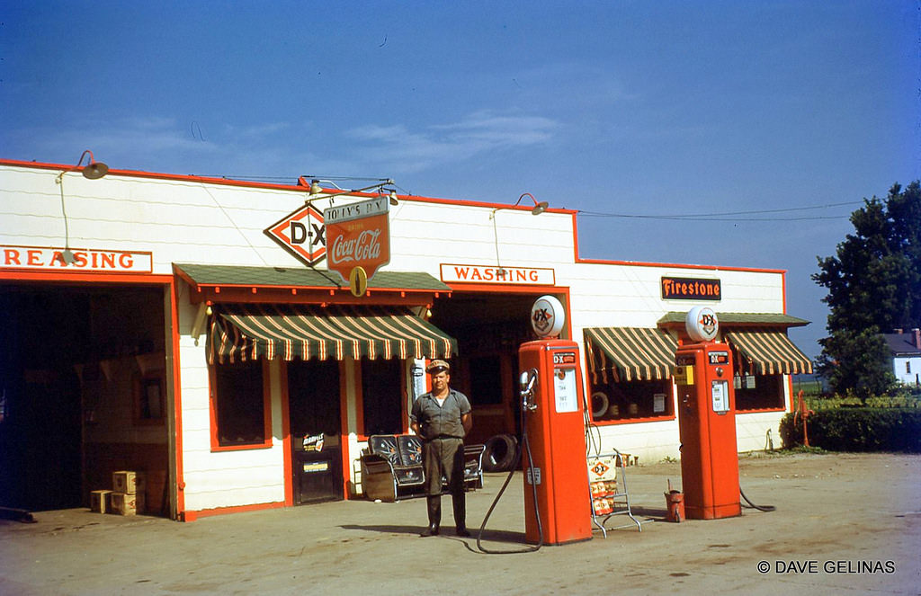 Tony's DX Gas Station with Coca Cola, Marvel Cigarettes, and Firestone Tires signs, and gas pumps with globes, in the Midwest, 1940s