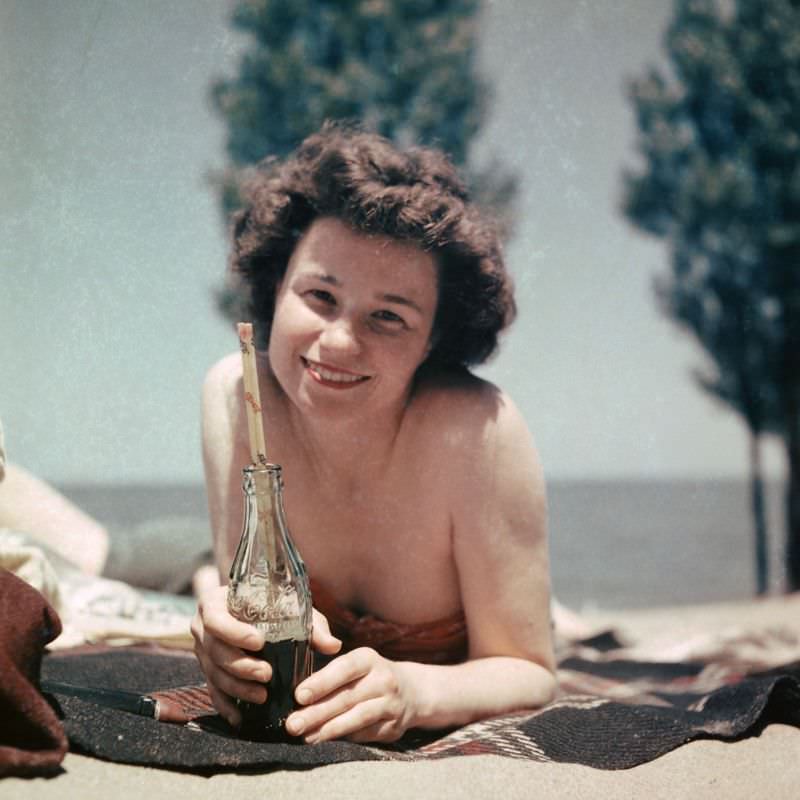 Girl with smile holding a Coke bottle while lying on the beach