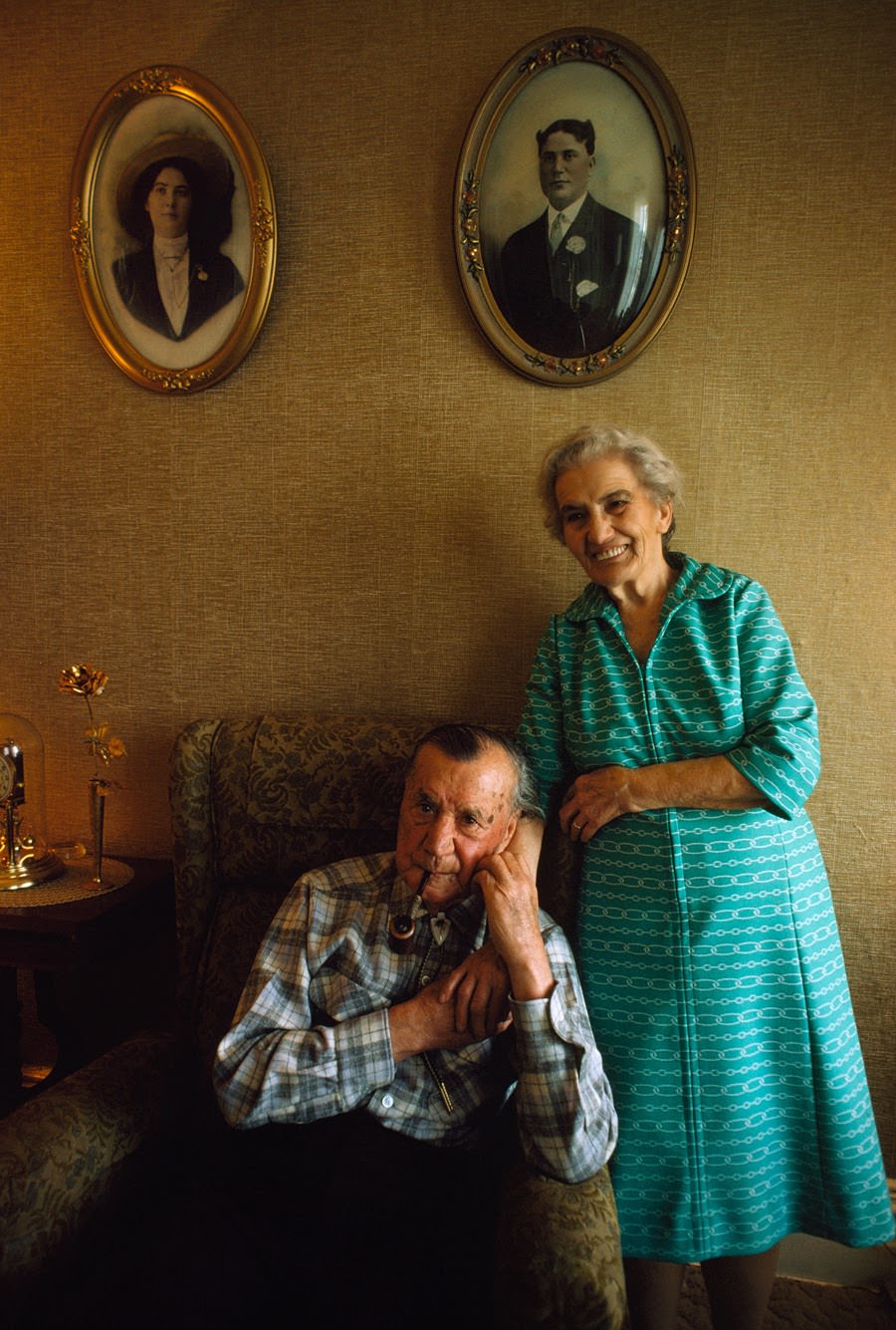 Elderly couple posing beneath their youthful portraits in Virginia City, Nevada, 1975
