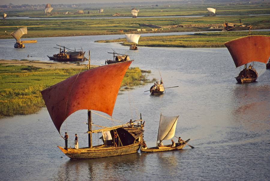 Red-sailed wood sailboats traveling the winding Turag River in Bangladesh, 1972
